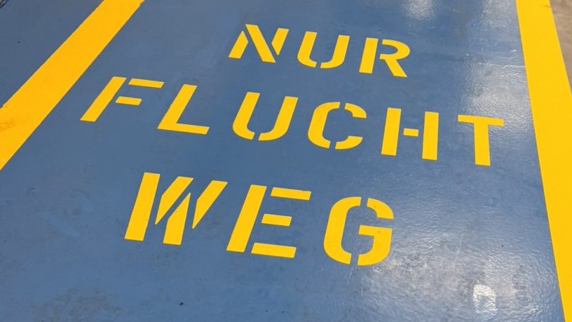 Fluchtwegmarkierung Gelbe Schrift auf blauem Boden: „NUR FLUCHT WEG“.