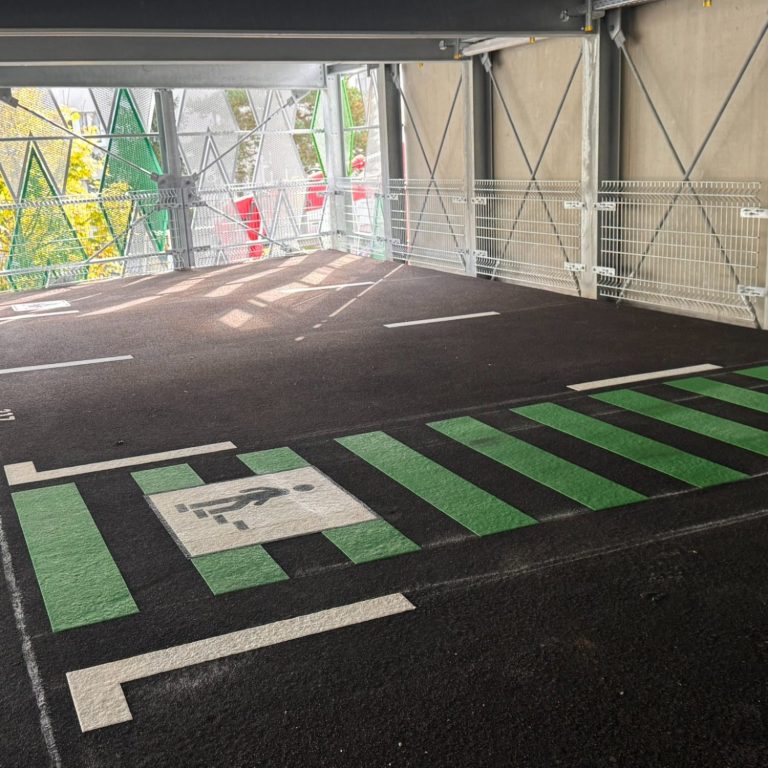 Parkhäuser ein graues Parkdeck, ein grüner Fußgängerüberweg, weiße Markierungen und ein weißes Symbol mit einem treppensteigenden Menschen