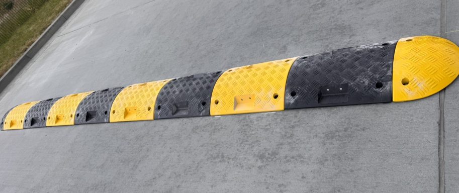 Gelber Bodenwellen-Hindernis auf grauem Asphalt, quer zur Fahrtrichtung angeordnet.