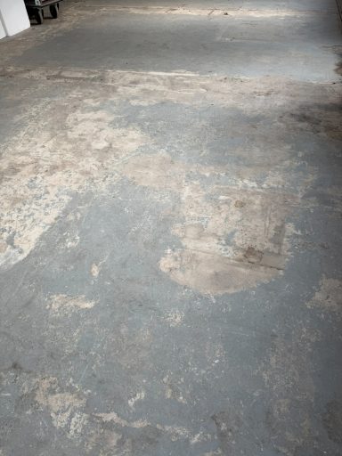 Abgenutzter, unebener Betonboden mit verfärbten Stellen und sichtbaren Rissen.