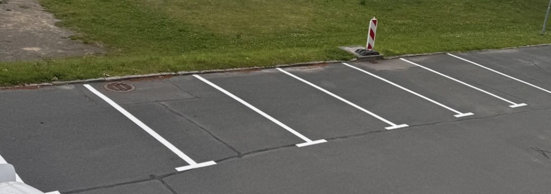 Leere Parkplätze mit weißen Markierungen und einer Absperrung am Rand.