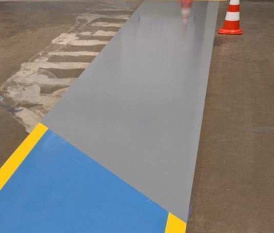 Staplerfahrwege Graue Bodenfläche mit blauer und gelber Linie, orange Verkehrscones im Hintergrund.