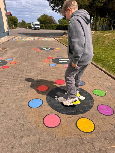 Junge steht auf einer bunten Bodenmarkierung auf einem Gehweg.