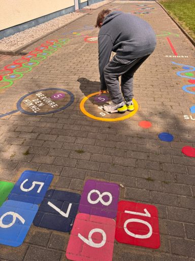 Ein Kind spielt auf einem bunten Hopscotch-Spiel auf dem Boden.