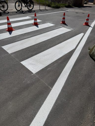 Weiße Zebrastreifen mit roten Verkehrshütchen auf asphaltierter Straße.