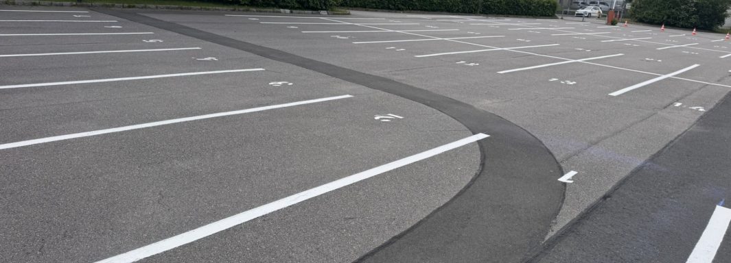 Leerer Parkplatz mit weißen Linien und einer leicht gebogenen Fahrbahn.