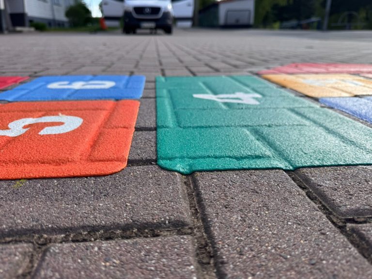 Bodenansicht eines bunten Hopscotch-Spiels auf einem Pflastersteinteppich.